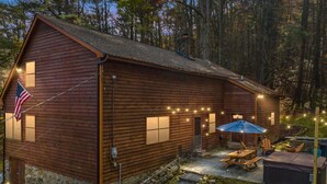 A rustic wooden cabin with a stone foundation, a patio with outdoor seating, and string lights.