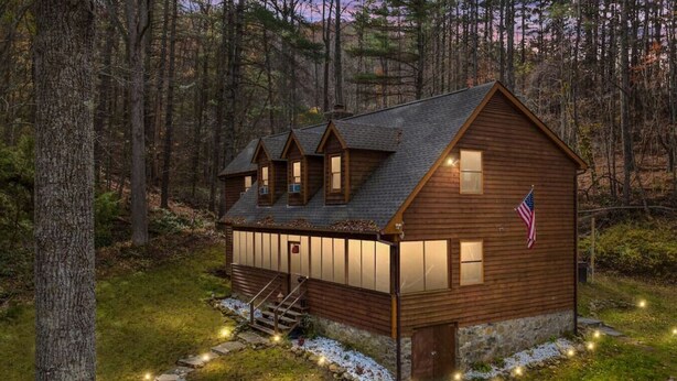 A wooden cabin with a stone foundation, a flag, and a porch with lights.