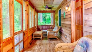 A wooden cabin with a porch, wicker furniture, and a ceiling fan.