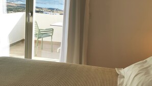 A hotel room with a bed, a view of the sea, and a balcony with a chair. - Kallisto Rooms (Milos)