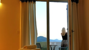 A hotel room with a bed, a table with chairs, and a view of the outdoors. - Kallisto Rooms (Milos)