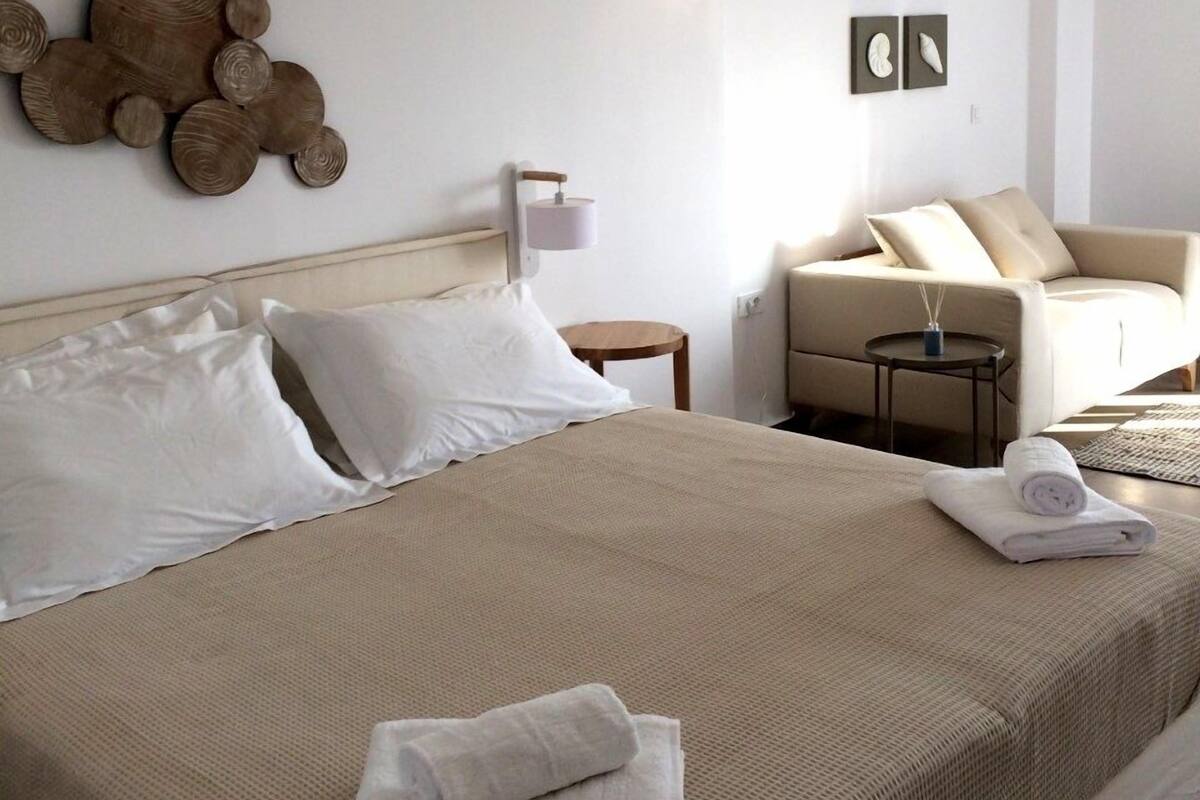 A hotel room with a large bed, a sofa, a small table, and wall art.