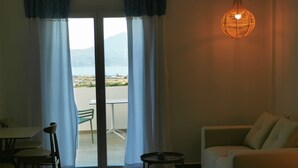 A room with a bed, a sofa, a table, and a chair. There is a view of a balcony with a table and chairs outside. - Kallisto Rooms (Milos)