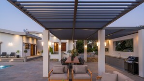 Un patio techado al aire libre con piscina, comedor y zona de barbacoa.