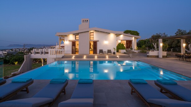 Una casa moderna con piscina, sillas de descanso y vistas al mar.
