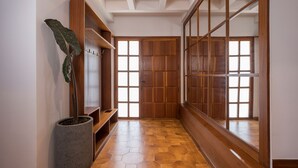 Un pasillo con piso de madera, una planta grande en maceta y una puerta de madera con paneles de vidrio.