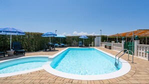 A swimming pool with two separate sections, surrounded by lounge chairs and umbrellas, and a brick patio.