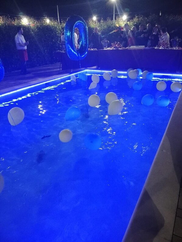 Une piscine éclairée de lumières bleues, avec des boules blanches et bleues flottant à la surface.