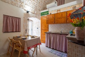 Une cuisine avec des meubles de rangement en bois, une table à manger recouverte d’une nappe à carreaux et un mur derrière l’évier recouvert de carreaux.