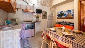 A kitchen with a microwave, oven, and sink; a dining table with chairs; and a painting on the wall.
