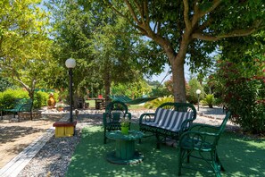 Un jardin avec un hamac, des chaises vertes, un banc et un lampadaire.