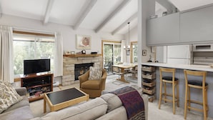 Una sala de estar con sofá, una mesa de centro, chimenea, televisor y una zona de cocina con barra y taburetes.