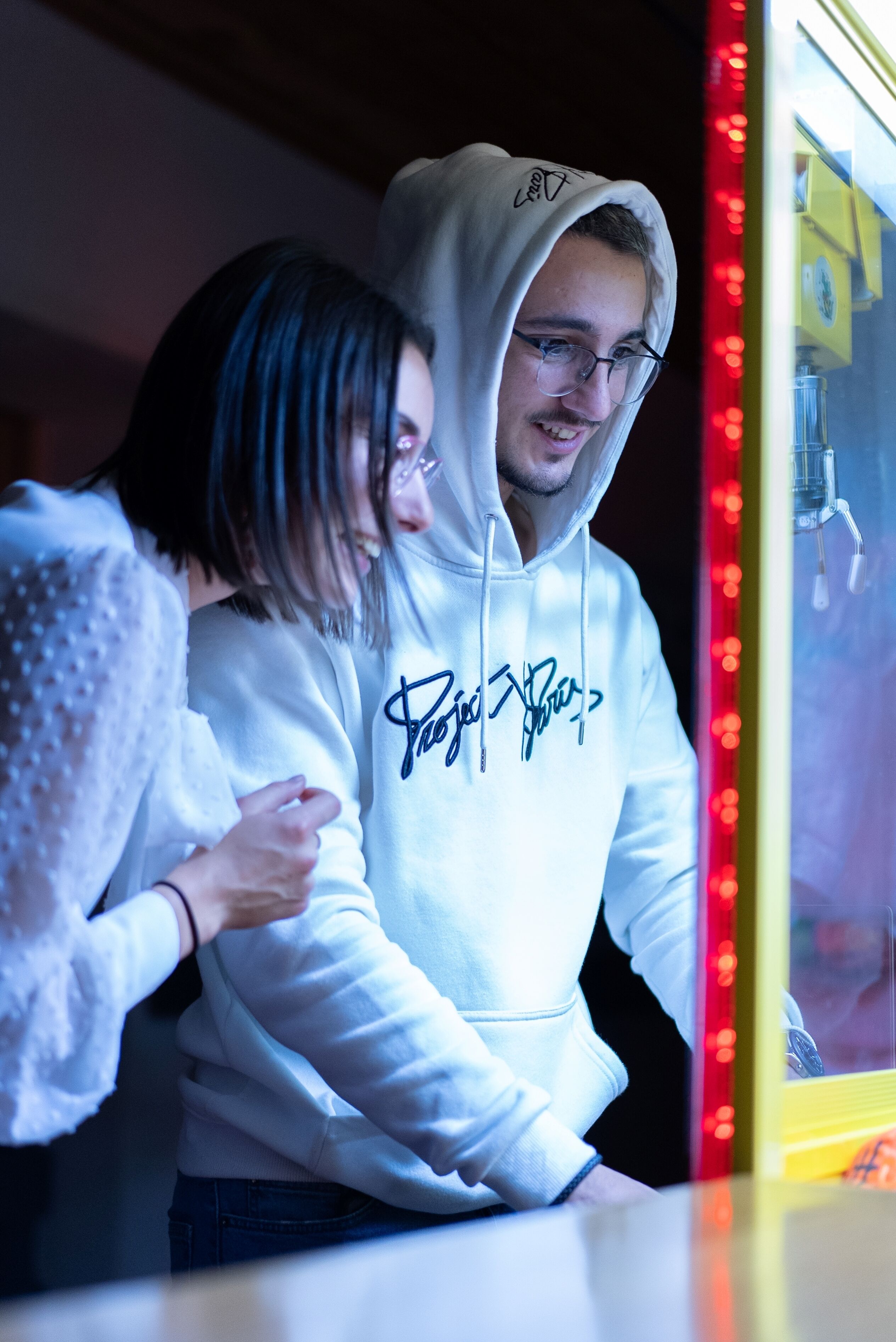 A person in a white hoodie with a signature on it, standing in front of a vending machine.