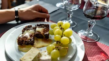 A plate with a dessert consisting of a chocolate cake with a creamy topping, a piece of white cheese, and a bunch of green grapes.