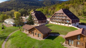 Un chalet moderne composé de plusieurs bâtiments en bois, d’une allée couverte et offrant une vue sur une chaîne de montagnes boisée.