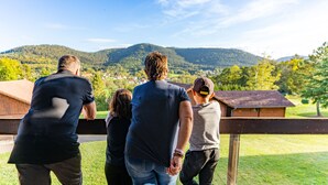Un groupe de personnes se tient sur une terrasse en bois, d’où l’on peut admirer un paysage pittoresque avec des collines et un petit village au loin.