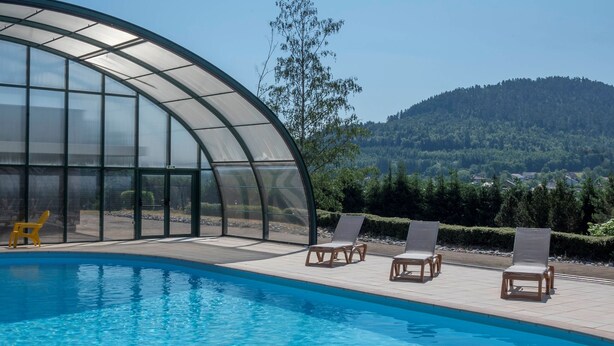 Une piscine à l’eau d’un bleu cristallin, entourée de chaises longues et abritée par une structure en verre.