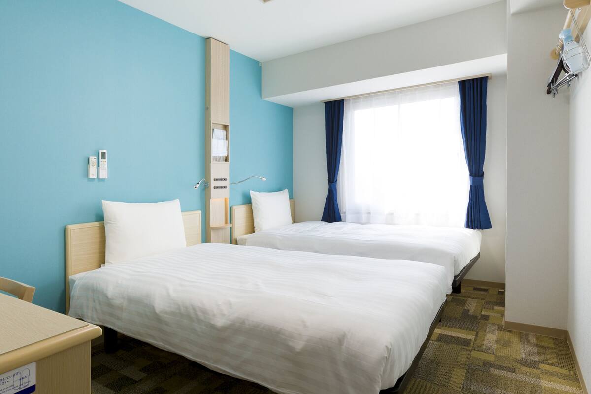 Ein Hotelzimmer mit zwei Betten, einem Schreibtisch und einem Fenster mit Vorhängen.