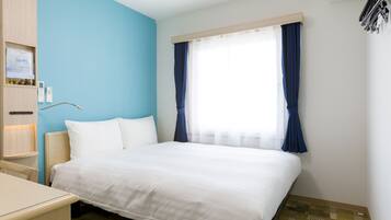A hotel room with a bed, bedside table, and a window with curtains.