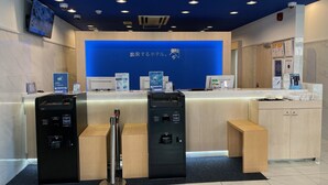 Un espace d’accueil avec un fond bleu, un comptoir et deux bornes de libre-service.