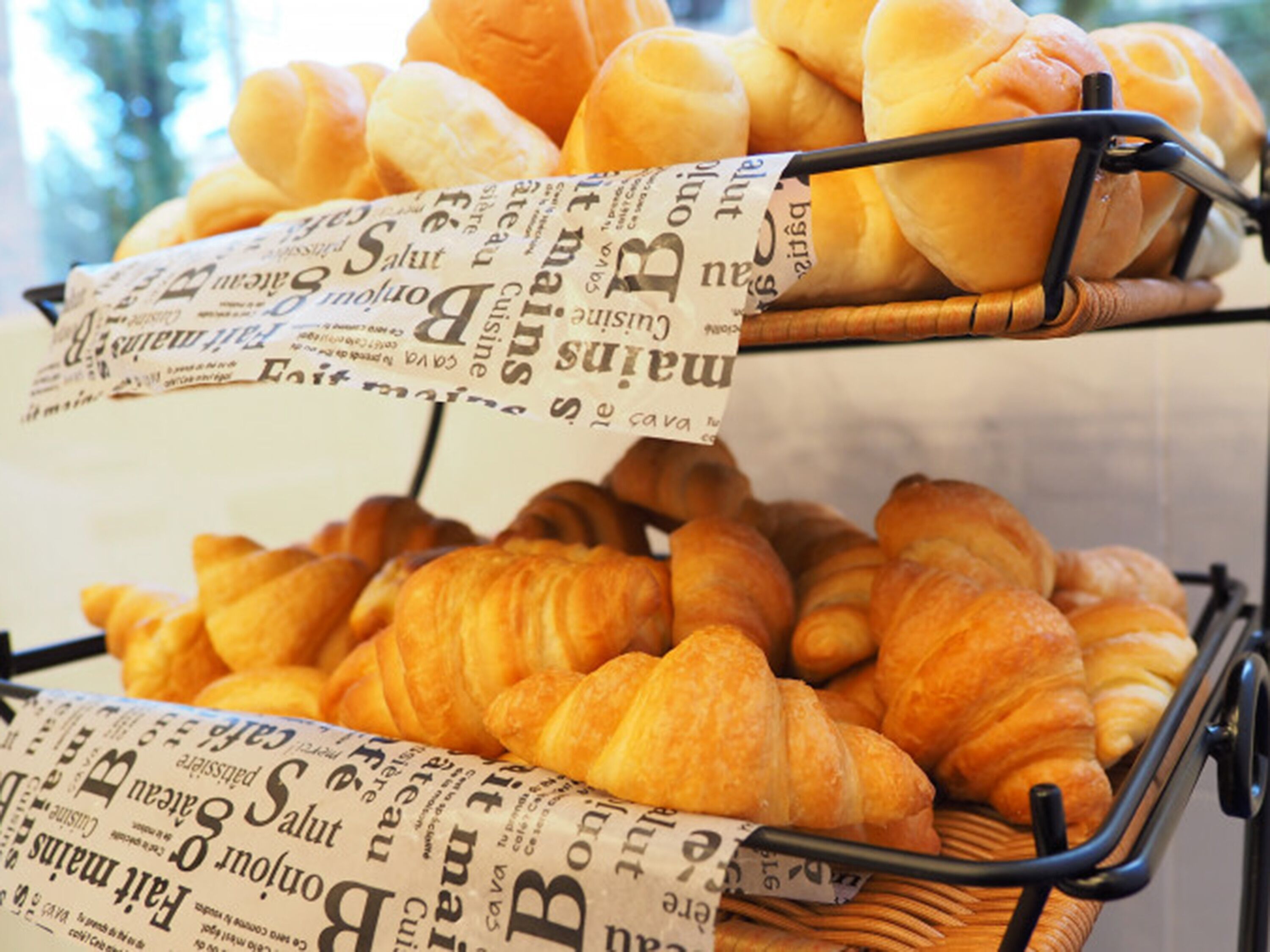 Uma cesta com croissants e uma baguete em uma grade de arame.