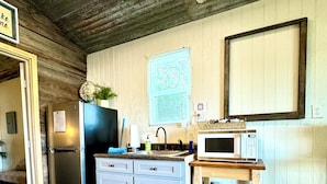 A compact kitchen with a refrigerator, sink, microwave, and wooden cabinets.