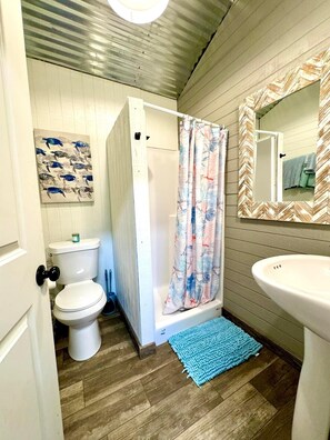 Un baño con inodoro, ducha, lavamanos y espejo con diseño de greca.