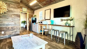 A rustic kitchen with wooden floors, a coffee table, bar stools, and a TV mounted on the wall.