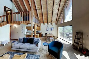 Un amplio salón con techo alto, una escalera, zona de comedor y grandes ventanales.