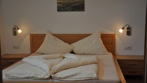 Ein ordentlich bezogenes Bett mit Holz-Kopfteil, zwei Nachttische mit Wandleuchten und ein kleines Bild an der Wand.