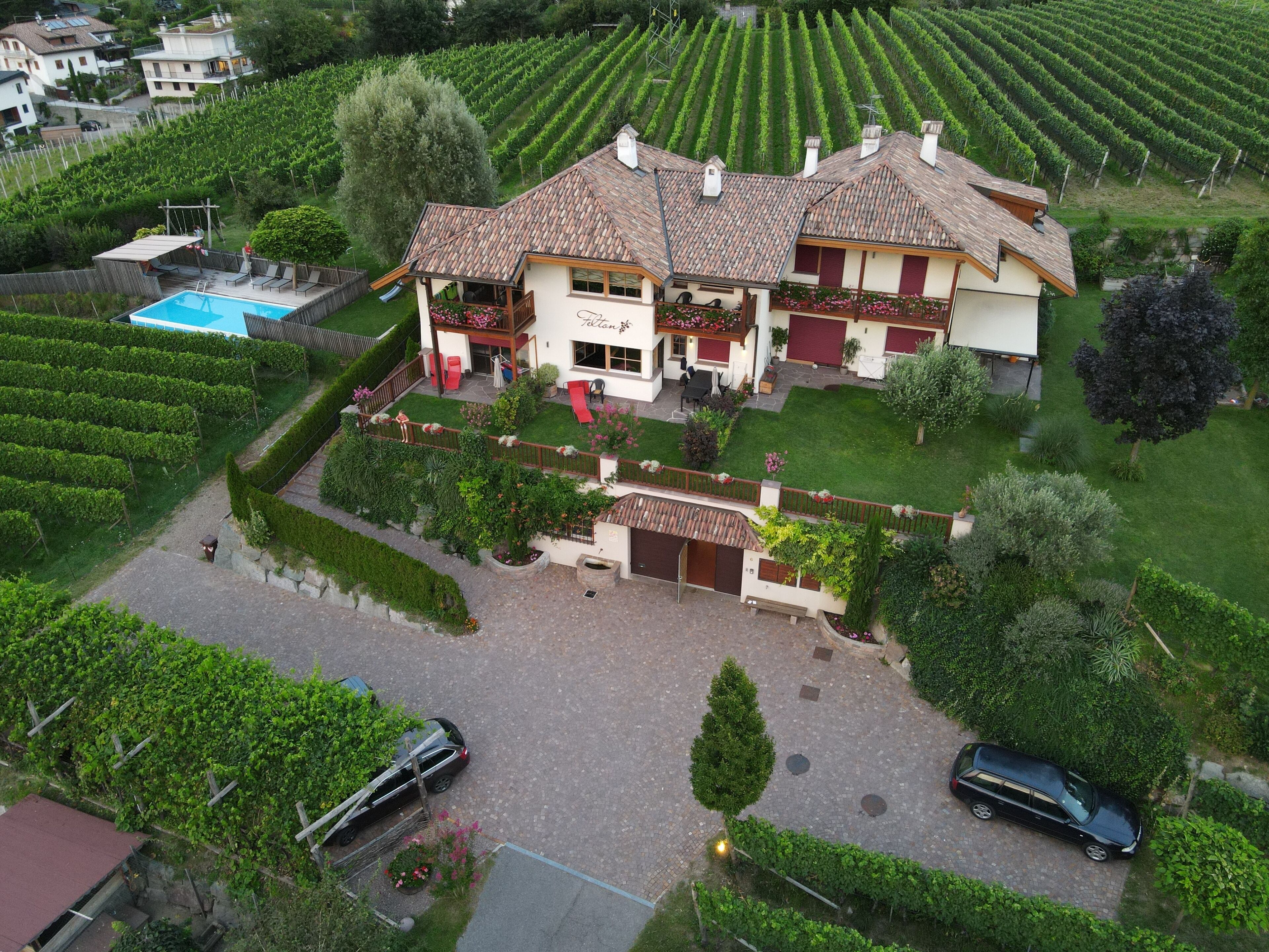 Ein zweistöckiges Haus mit einem Ziegeldach, umgeben von einem gepflegten Garten und einem Weinberg.