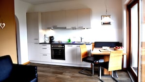 Eine kleine Küche mit weißen Schränken, einem eingebauten Backofen und einem Essbereich mit Holztisch und Stühlen.