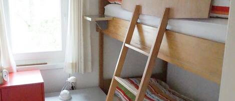 A bunk bed room with a ladder, a desk with a lamp, and a window with curtains.