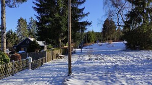 Un patio cubierto de nieve con una valla de madera, un banco y una casa.