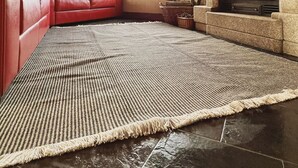Een ruime woonkamer met een rode leren bank, een geweven vloerkleed, een open haard en een groot raam.