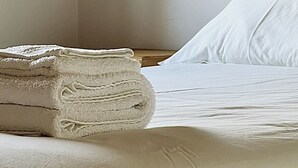 Een opgemaakt bed met witte lakens en een gevouwen handdoek op de zijkant.