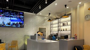 Eine moderne Hotelhalle mit einer Rezeption, einer Sitzecke und einem Fernseher, der ein Basketballspiel zeigt.