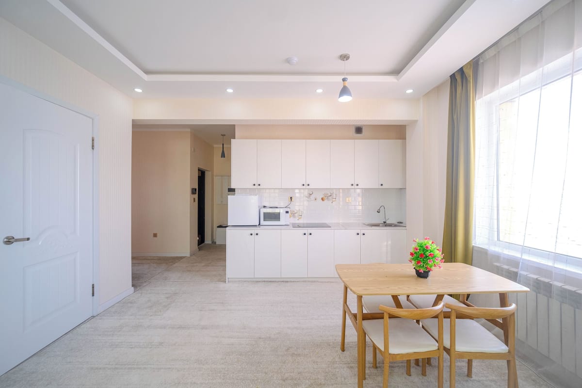 A modern kitchen with white cabinets, a microwave, and a dining area with a wooden table and chairs.