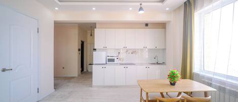 A modern kitchen with white cabinets, a microwave, and a dining area with a wooden table and chairs.