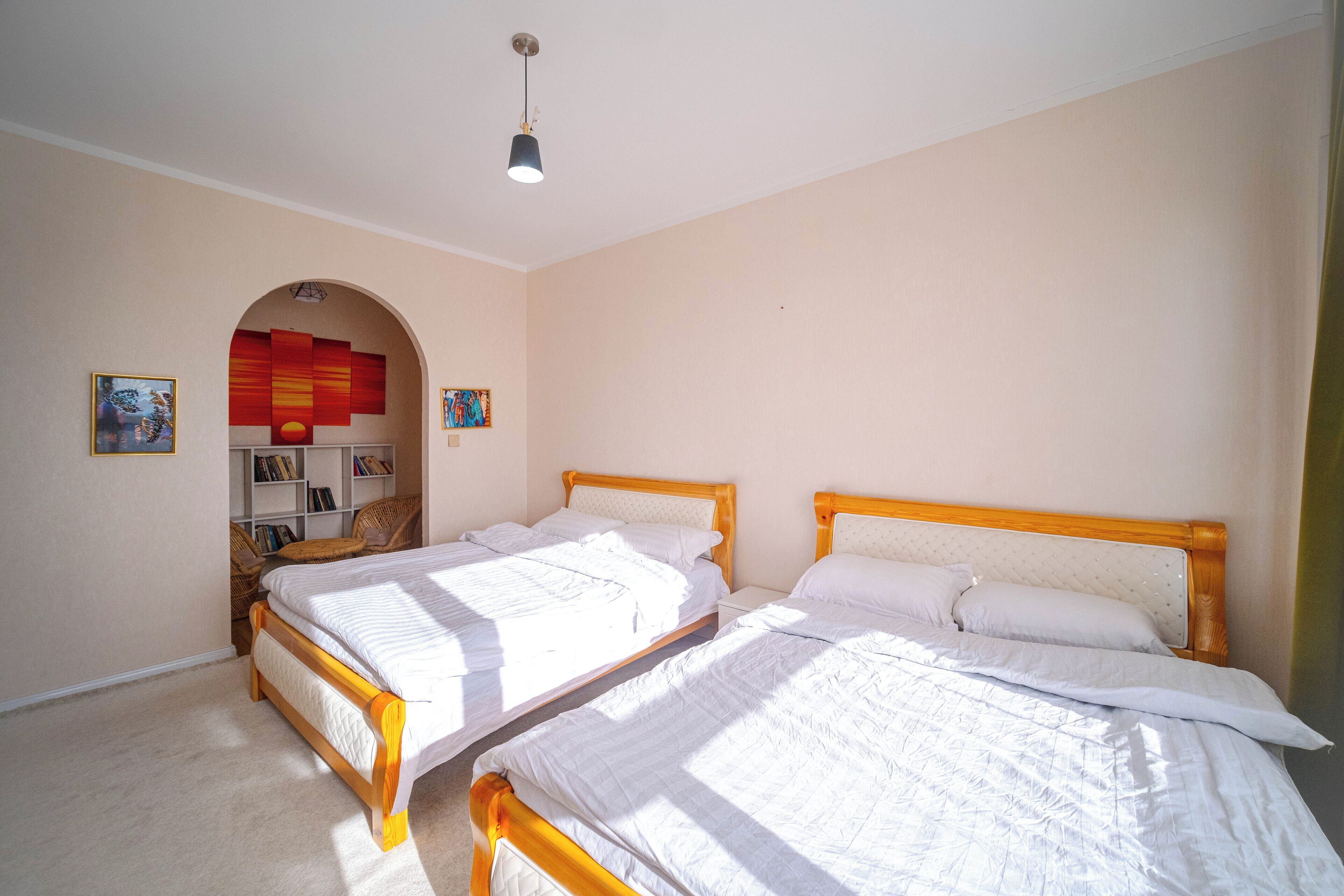 Un dormitorio con dos camas, una estantería y un pequeño rincón de descanso.