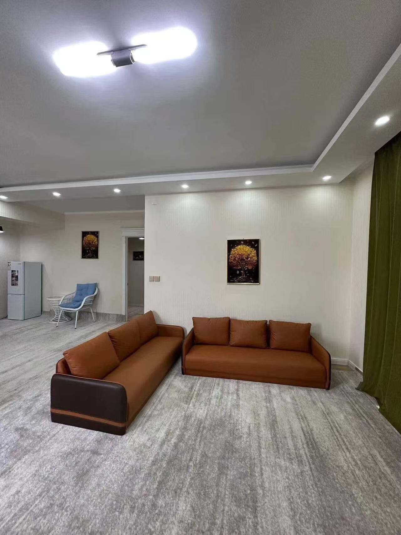 A spacious living area with two brown sofas, a white chair, and a ceiling fan.