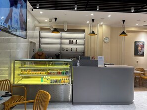 L'intérieur d'un café moderne présente un présentoir rempli de collations, un comptoir avec une caisse enregistreuse et un espace salon avec des chaises et des tables.