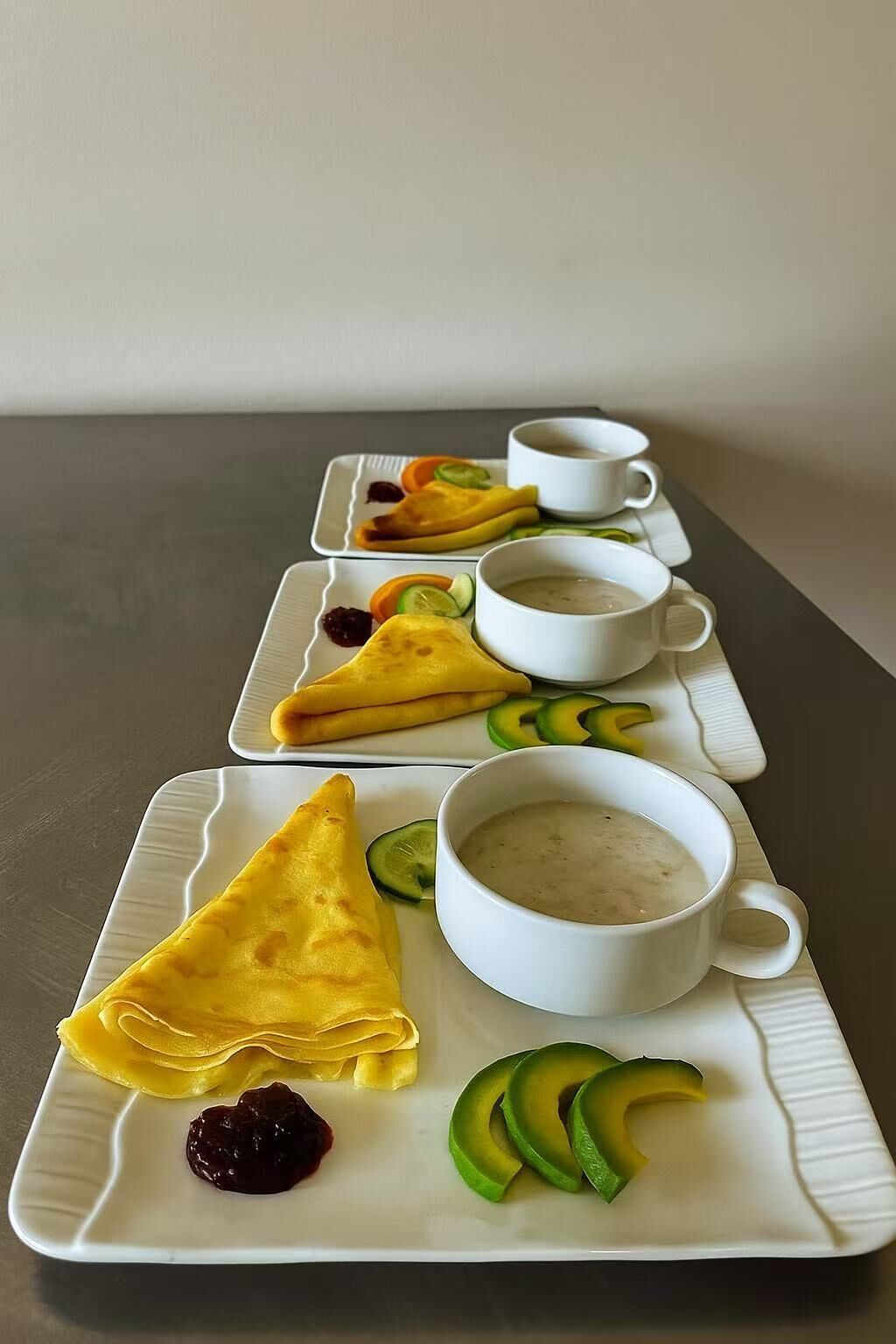 A breakfast tray with pancakes, avocado slices, and a bowl of soup.
