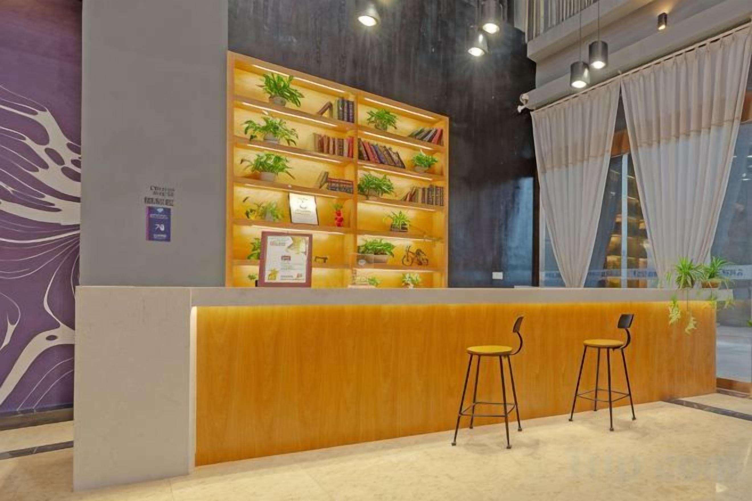 Una zona de recepción con mostrador de madera, dos taburetes de bar y una estantería con plantas.