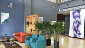 A modern lobby with a blue wall, a wooden reception desk, a red sofa, teal armchairs, and several potted plants. - LANOU Hotel (Haiyan Science City) (Haiyan)