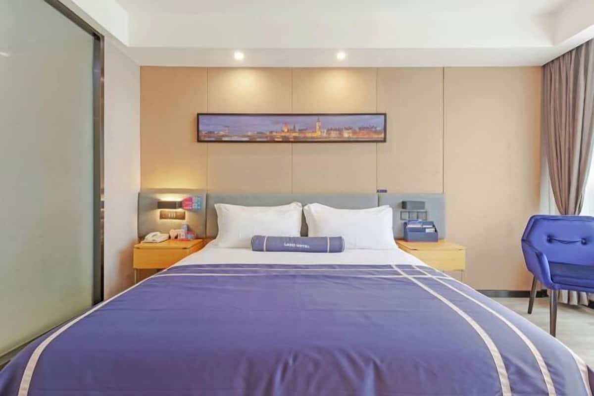 A hotel room with a bed, a nightstand with a phone, a lamp, and a chair.