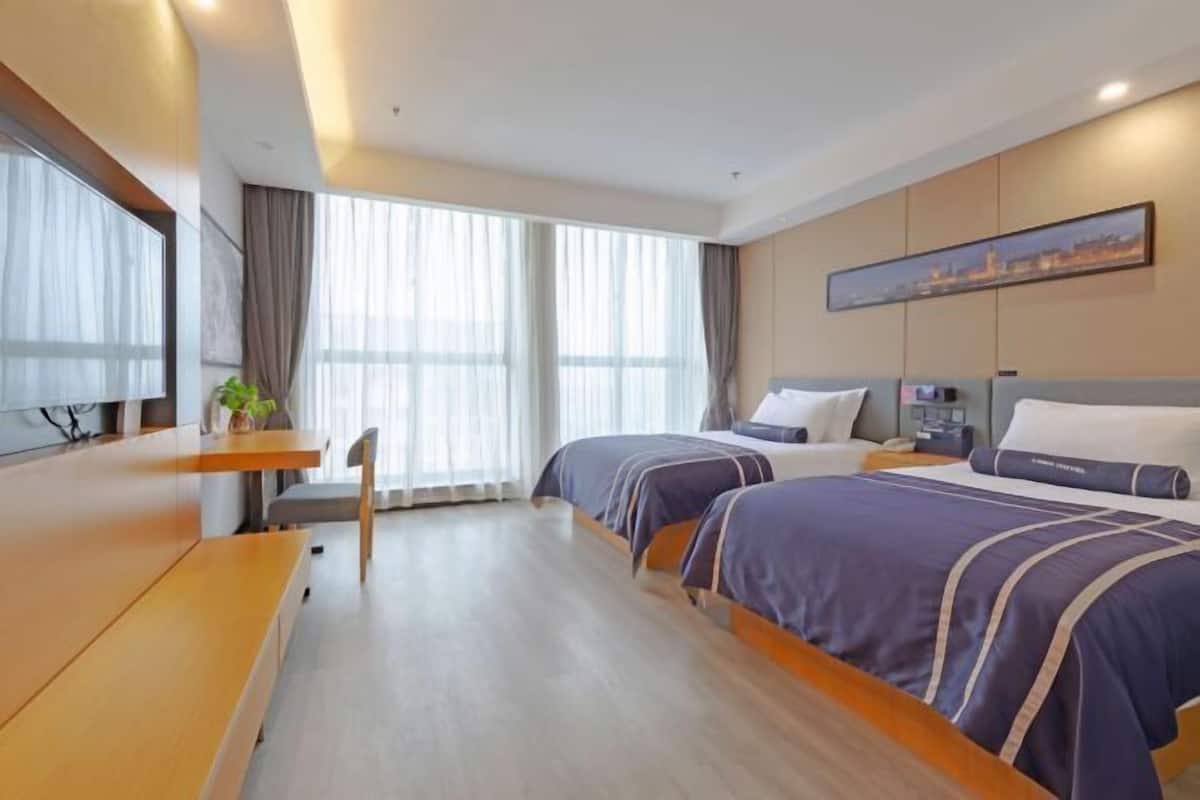 A hotel room with two beds, a desk, and a large window with curtains.