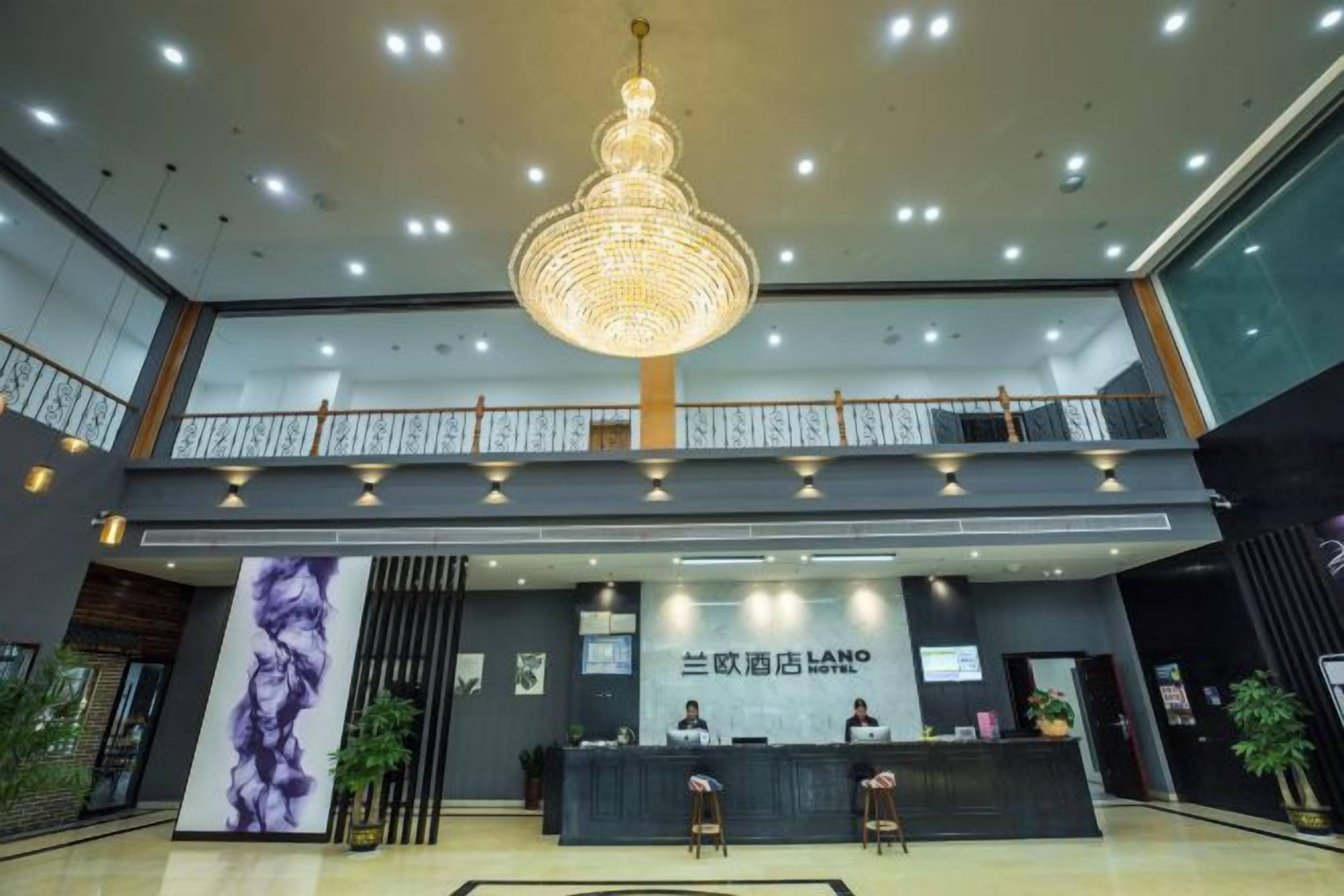 A hotel lobby with a reception desk, a chandelier, and a balcony.