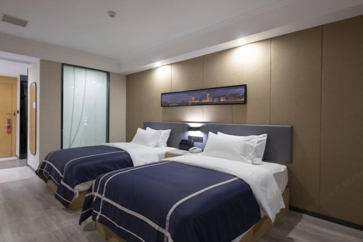 A hotel room with two beds, a nightstand, a wall-mounted TV, and a cityscape painting.