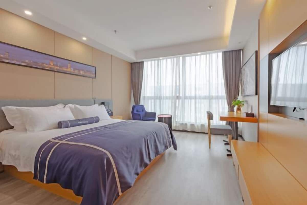 A modern hotel room with a large bed, a desk, a chair, and a television.